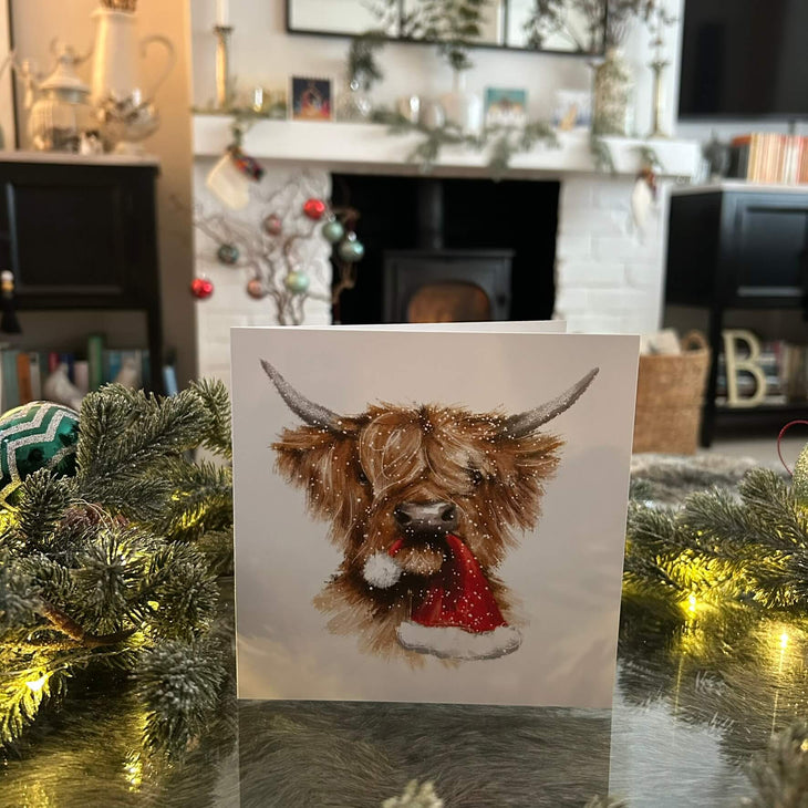 Highland cow with Christmas hat in its mouth
