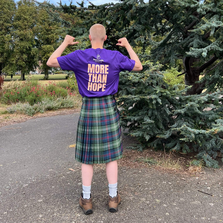 Tom, with his back to the camera, wearing his kilt and a purple tshirt with More Than Hope written on the back